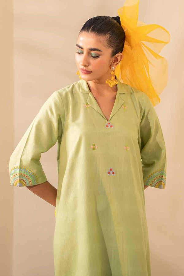 A woman in a light green jacquard shirt adorned with yellow flowers, radiating elegance and natural beauty.