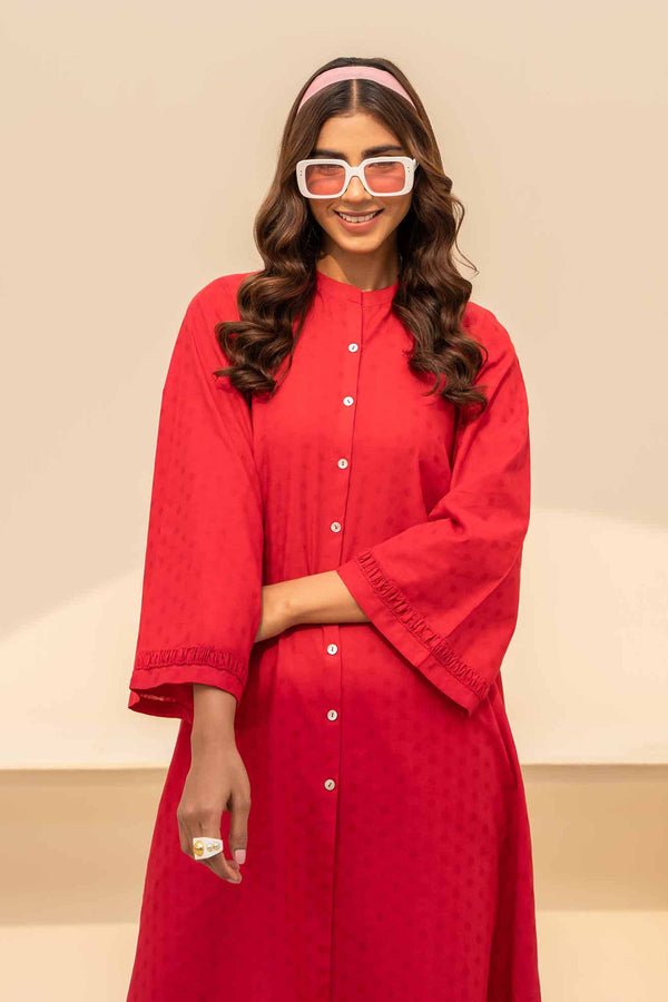 A woman in a red jacquard shirt and cambric trousers, radiating style and confidence.